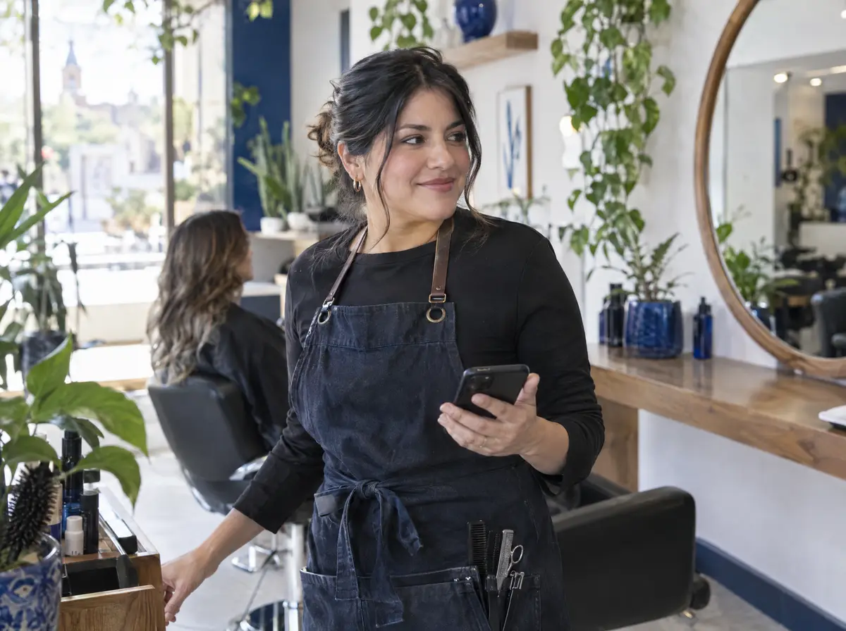 Estilista en una estética revisando su celular entre clientas